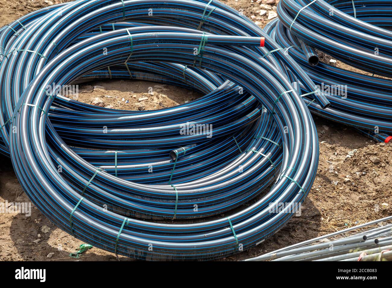 Schwarze PVC-Schläuche mit blauen Linien. Polyethylenschläuche, Rohrmaterial auf der Baustelle. Stockfoto