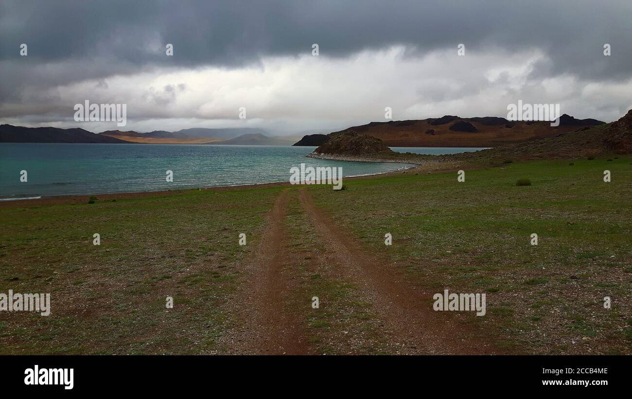 Eine unbefestigte Straße, die in Richtung eines blauen Sees im Norden führt Mongolei unter einem bewölkten Himmel Stockfoto