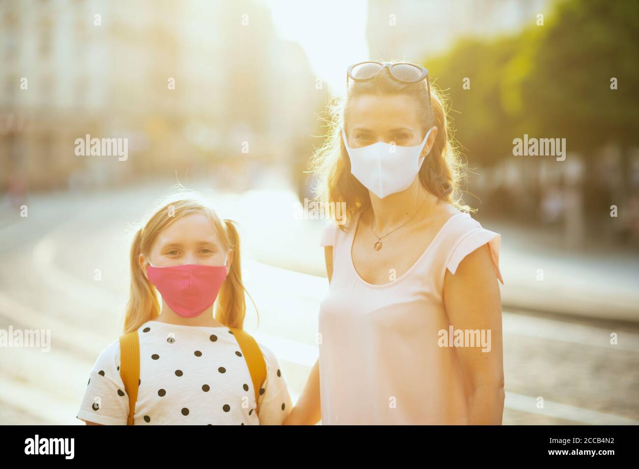 Leben während der covid-19 Pandemie. Portrait von eleganten Mutter und Kind mit Masken und gelben Rucksack immer bereit für die Schule draußen. Stockfoto