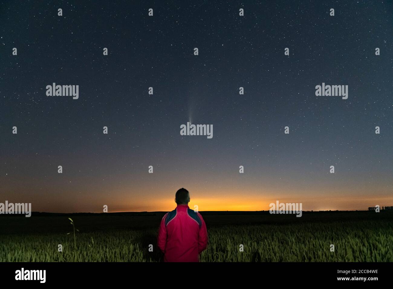 Silhouette eines Mannes, der nachts auf einem Feld außerhalb der Stadt steht. Sternenhimmel mit Komet Neowise C/2020 F3 Stockfoto