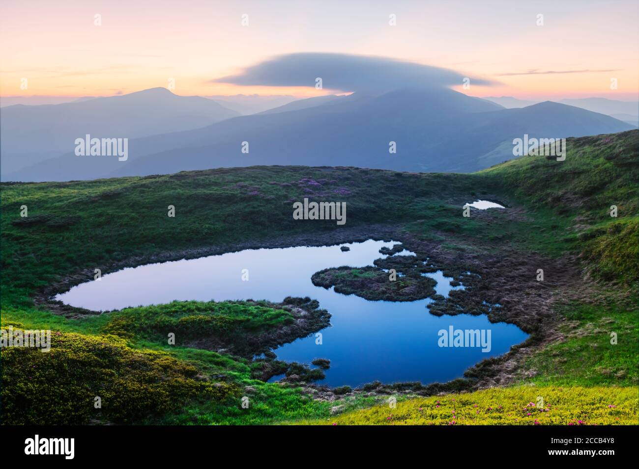 Bergsee bei Sonnenaufgang. Malerische Sommerlandschaft mit grünen Hügeln und Sonnenstrahlen am Morgenhimmel. Karpaten Stockfoto