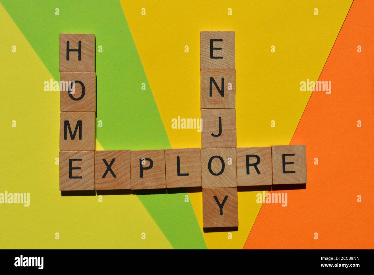 Startseite, Genießen, Erkunden, Wörter in hölzernen Alphabet Buchstaben in Kreuzworträtsel-Form isoliert auf bunten Hintergrund Stockfoto