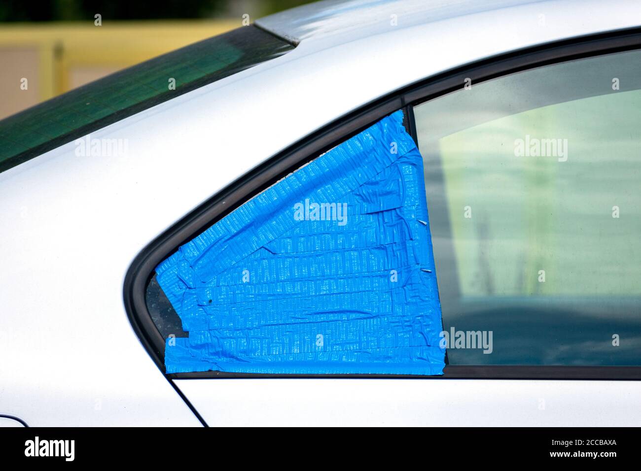 Kaputtes und beschädigtes Autofenster, das vorübergehend mit blauem Klebeband bedeckt ist, um das Innere vor Regen und Wasser zu schützen. Smash-and-Grab Automobil-Einbrüche. Stockfoto