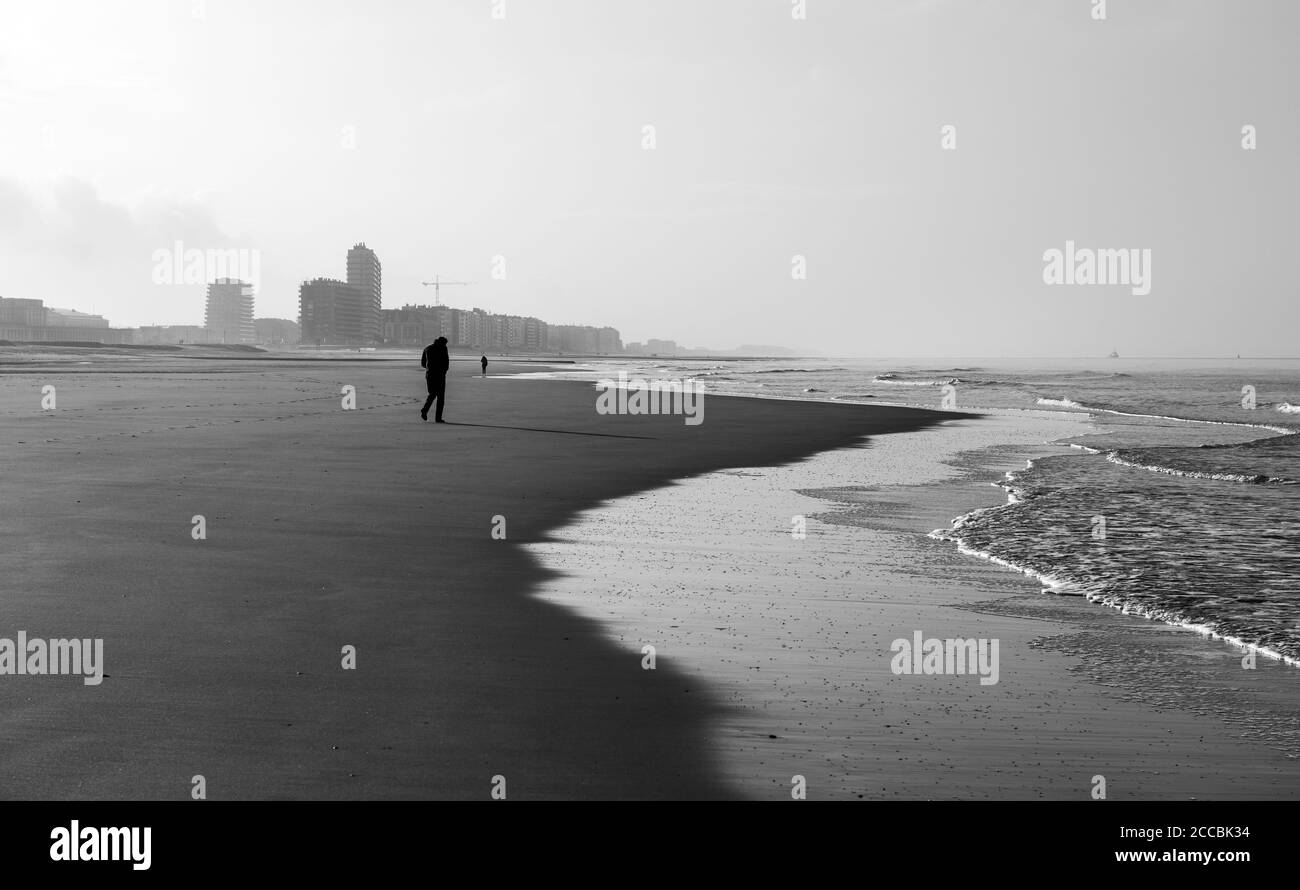 Einsamer Mann beim Spaziergang am Strand von Oostende (Ostende) Stadt an der Nordsee in schwarz-weiß, Belgien. Stockfoto