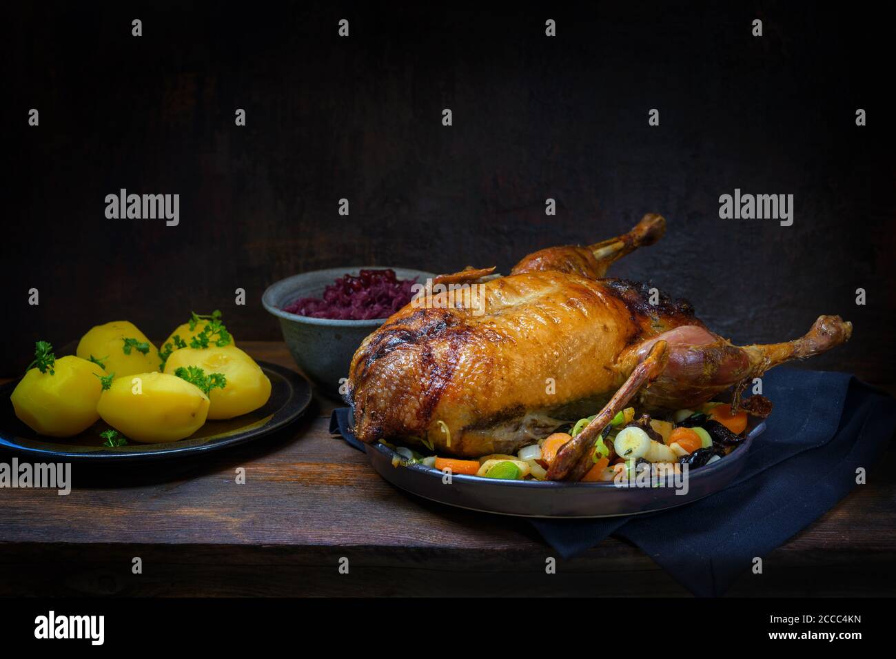 Geröstete Ente mit Kartoffeln und Rotkohl, ein festliches Essen auf einem rustikalen Holztisch, dunkelbrauner Hintergrund mit Kopierraum, ausgewählter Fokus, schmaler Abgang Stockfoto