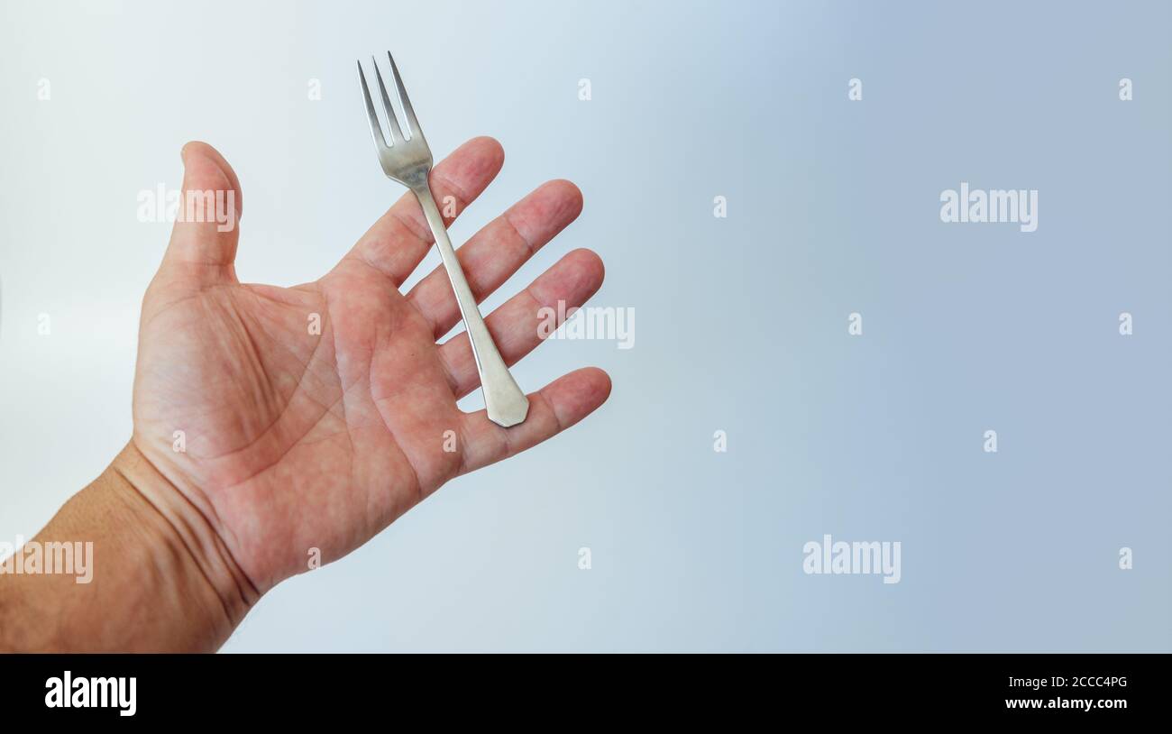Kleine Stahlgabel in der Handfläche des Menschen, isoliert auf weißem Hintergrund. Kopierraum Stockfoto