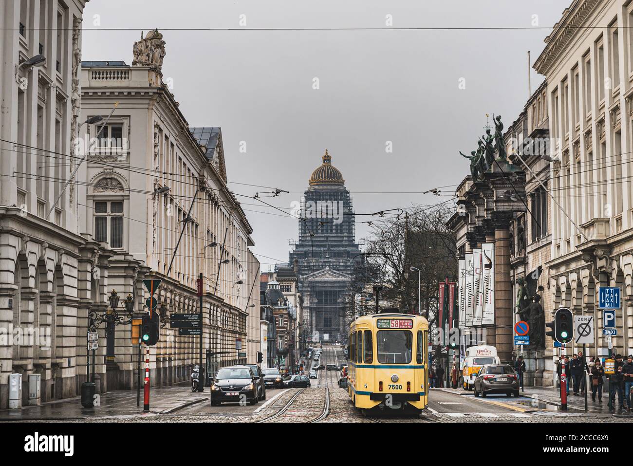 Eine traditionelle gelbe Straßenbahn, die die geschäftige Straße Rue de la Regence mit dem imposanten Justizpalast (Brüsseler Gerichtshof) überquert Stockfoto