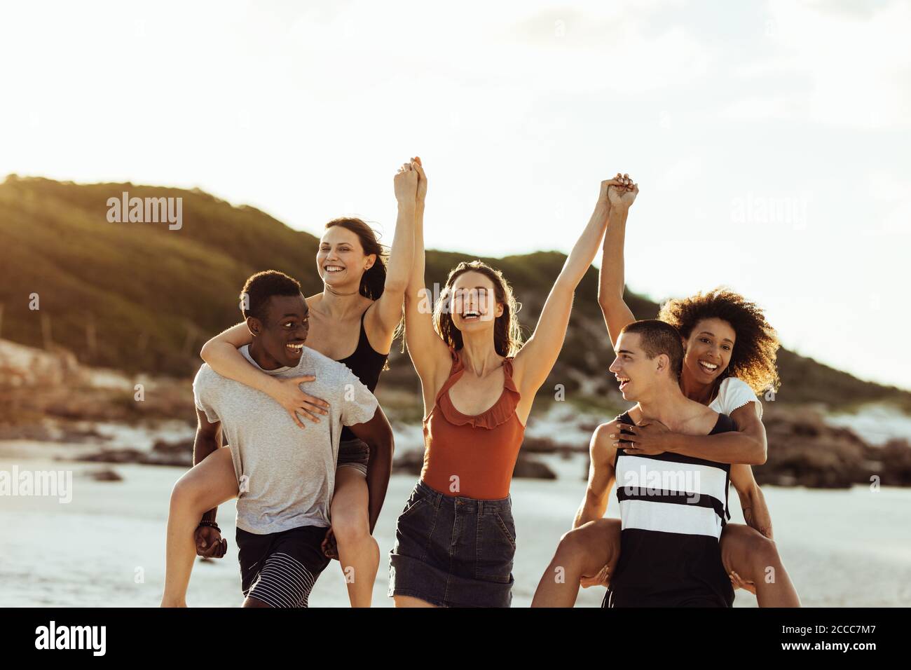 Multiethnische Freunde in verspielter Stimmung am Strand genießen. Fröhliche Männer und Frauen mit Spaß genießen Piggy Reiten. Stockfoto