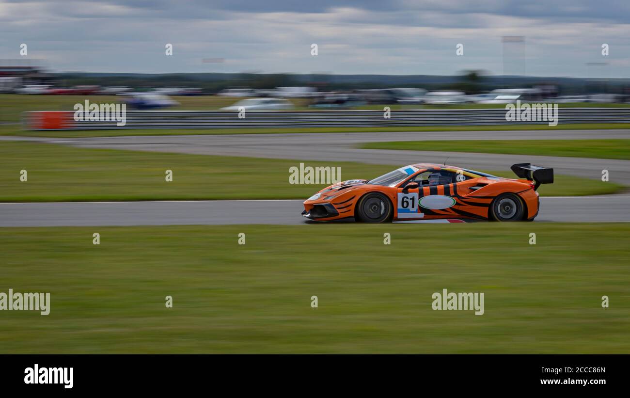 Eine Schwenkaufnahme eines schwarzen und orangen Rennwagens, der auf einer Rennstrecke fährt. Stockfoto