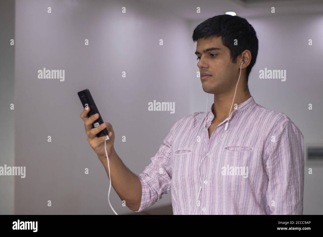 Indischer Mann, der sein Handy mit Kopfhörern in den Ohren benutzt Stockfoto