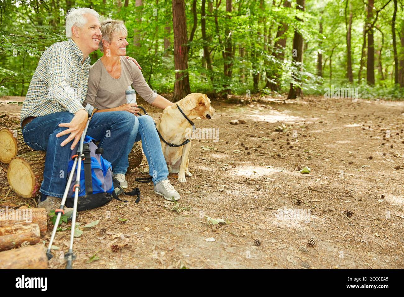 Zwei glückliche Senioren mit Hund machen eine Pause Der Wald Stockfoto