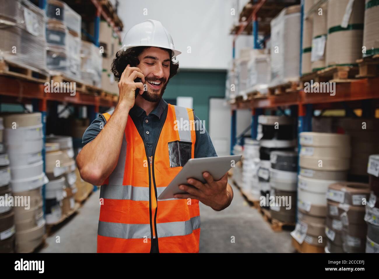 Erfolgreicher Werksleiter, der Versanddetails mit einem digitalen Tablet verfolgt, während Im Gespräch über Smartphone im Lager Stockfoto