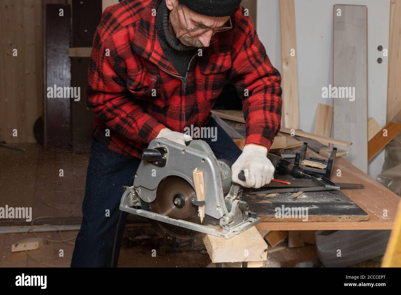 In seiner Werkstatt arbeitet ein älterer Herr als Zimmermann mit Kreissäge. Aktives Alter Stockfoto