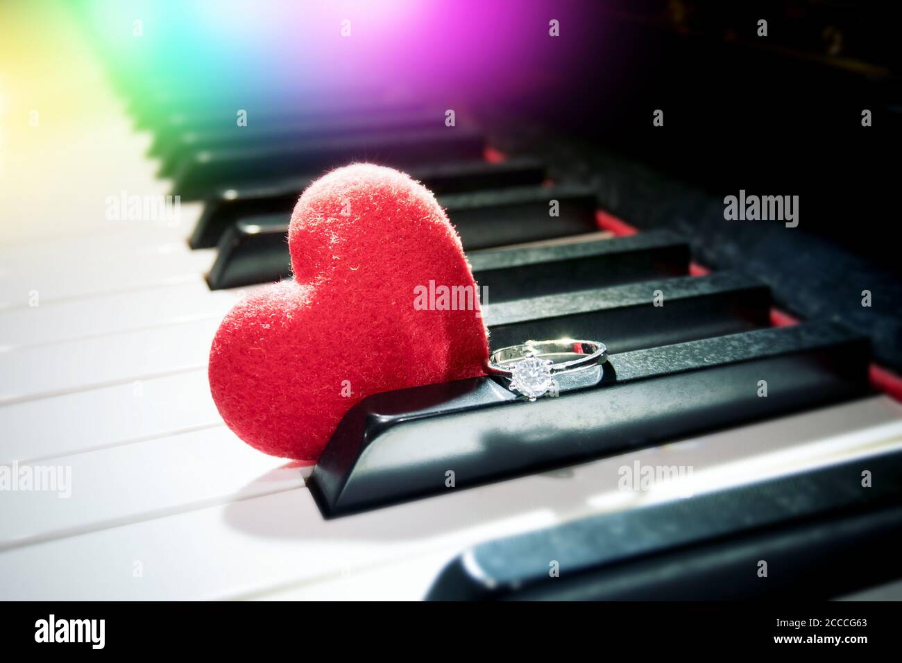 Romantisches Beziehungskonzept: Samtrotes Herz und glänzender Diamantring am Klavier Stockfoto