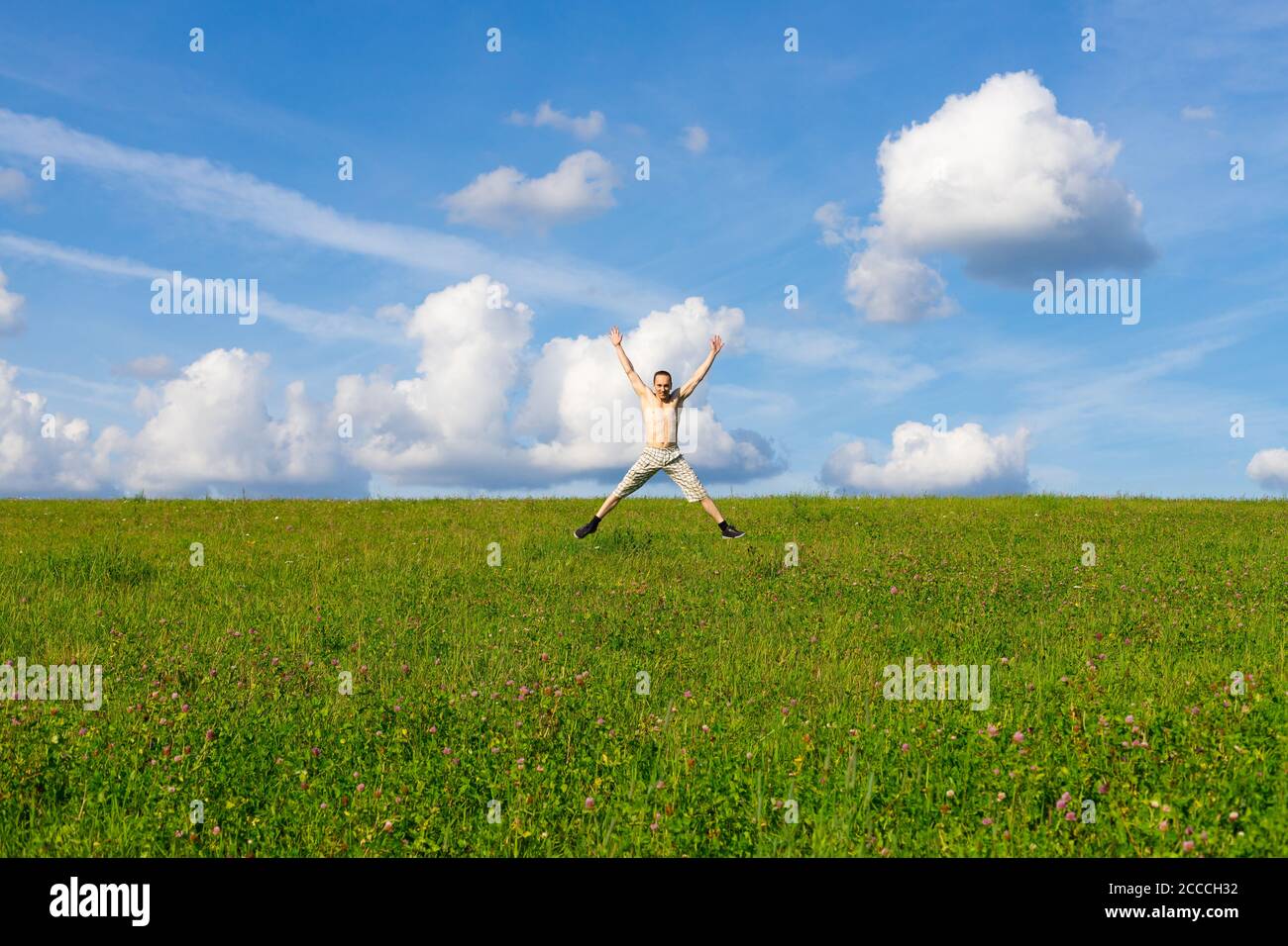 Mann springt auf Wiese auf schönen blauen Himmel und weiß Wolken Hintergrund Stockfoto
