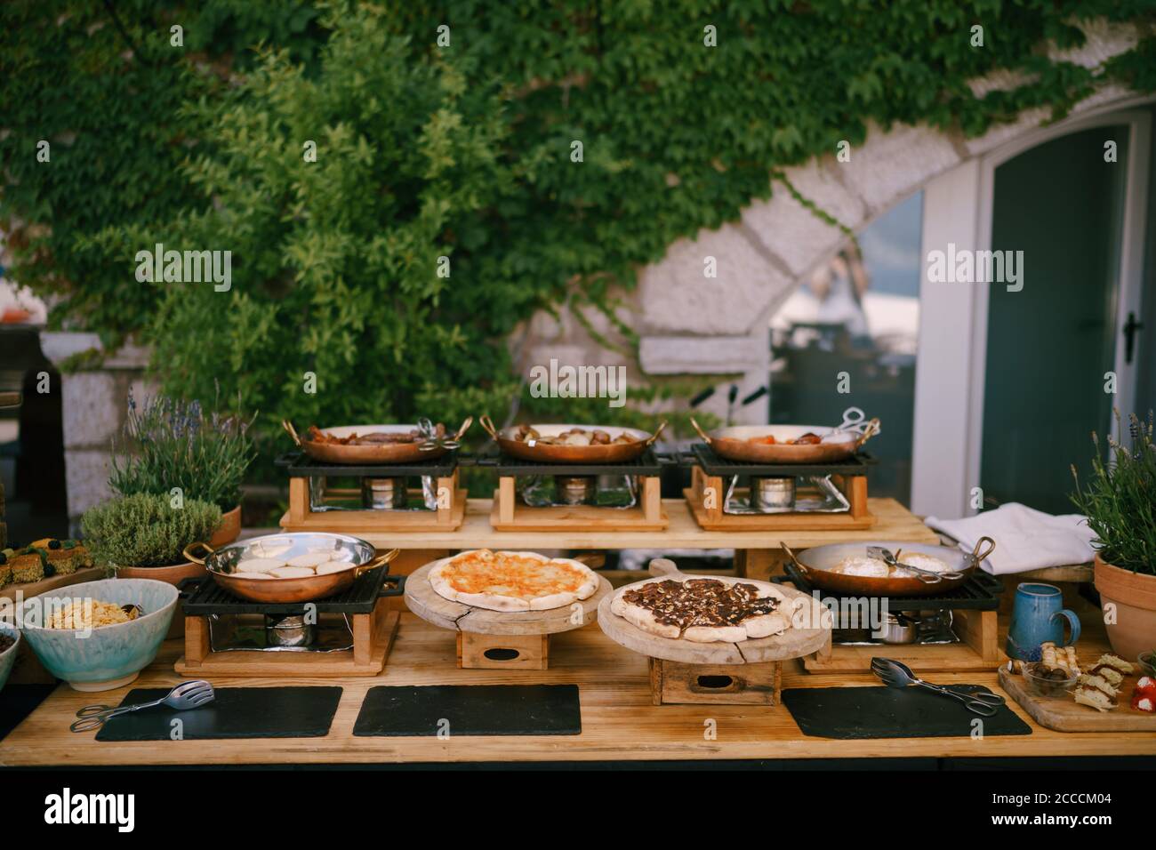 Küche mit Pfannen und Holzbretter für Pizza mit Speisen für ein Bankett im Hintergrund eines Gebäudes mit Grünflächen vorbereitet servieren. Stockfoto