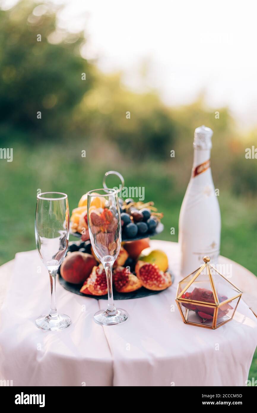 Ein Tisch mit weißer Tischdecke und zwei Sektgläsern und ein Bücherregal mit Früchten in der Natur. Stockfoto
