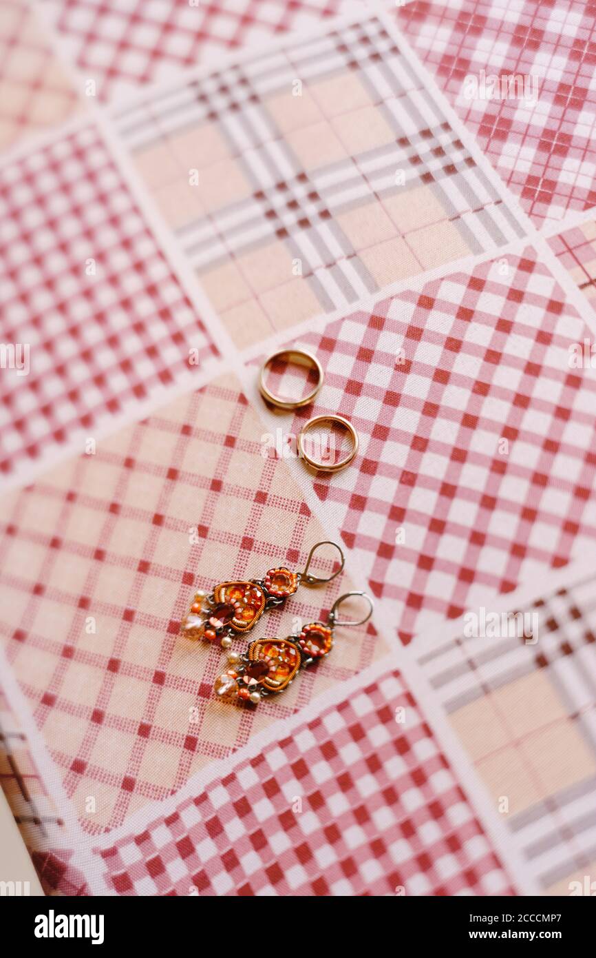 Budva, Montenegro - 21. august 2020: Goldene Eheringe. Ohrringe mit Steinen und goldenen Eheringen auf kariertem Stoff. Stockfoto