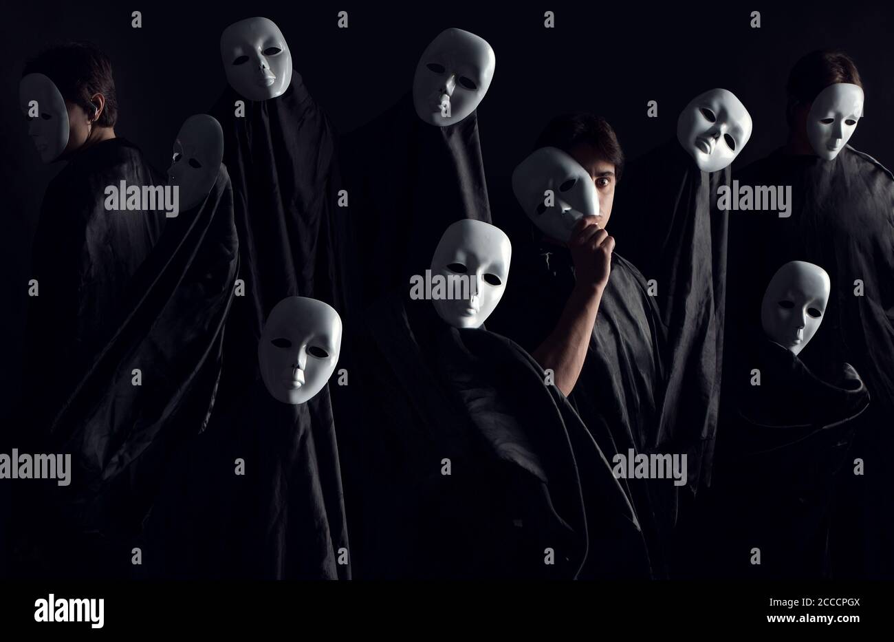Figurengruppe in schwarzen Gewändern und weißen Masken, wie auf einem Kult. Einer von ihnen blickt mit einem Auge direkt auf die Kamera. Stockfoto