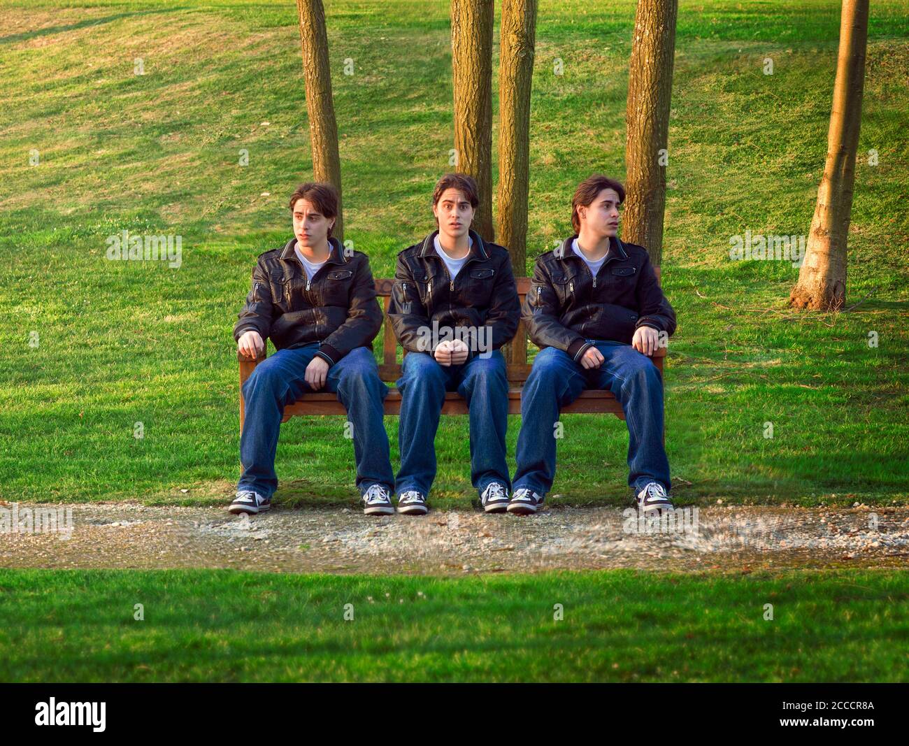 Drei Klone desselben Mannes, der auf einer Bank sitzt Stockfoto