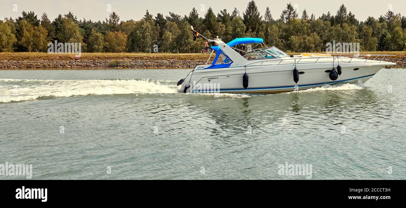 Gifhorn, 9. August 2020: Weißes Motorboot mit blauem Dach bewegt sich mit hoher Geschwindigkeit durch den Kanal mit spritzendem Wasser Stockfoto