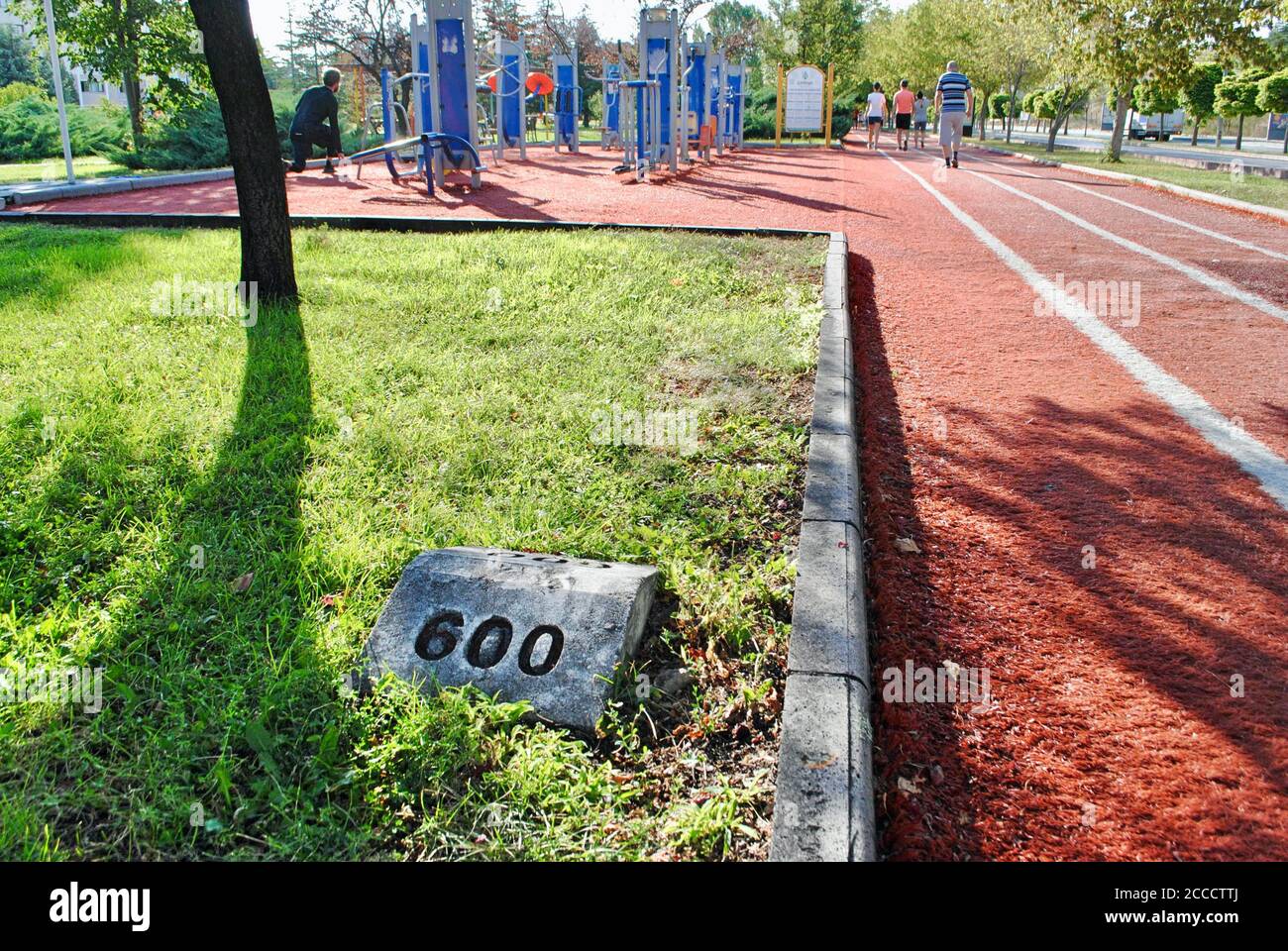 Menschen zu Fuß und tun Bewegung auf dem Gleisfeld mit Kilometeranzeige im Gras und Stahl Geräte für Fitness. Fitnesskonzept im Freien. Stockfoto