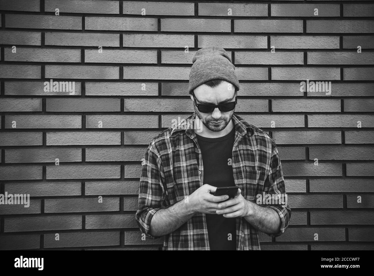 Hipster sms SMS SMS-SMS-Handy-App in der Stadt Straße auf Backsteinmauer Hintergrund. Erstaunlich Mann hält Smartphone in smart Casual wear stehen. Stockfoto