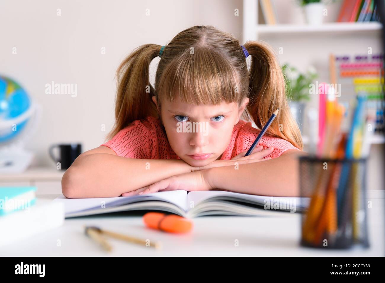 Kleines Mädchen, das zu Hause studiert, wütend mit gekreuzten Armen Buchen Sie am Schreibtisch zu Hause Stockfoto