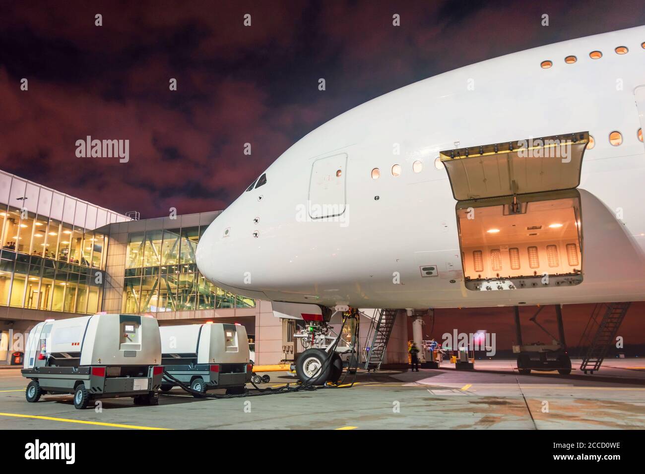 Nachts geöffnete Gepäckraumtür eines Passagierflugzeugs in der Nähe des Flughafenterminals. Blick auf die Nase und das Cockpit mit elektrischen Installationen Stockfoto