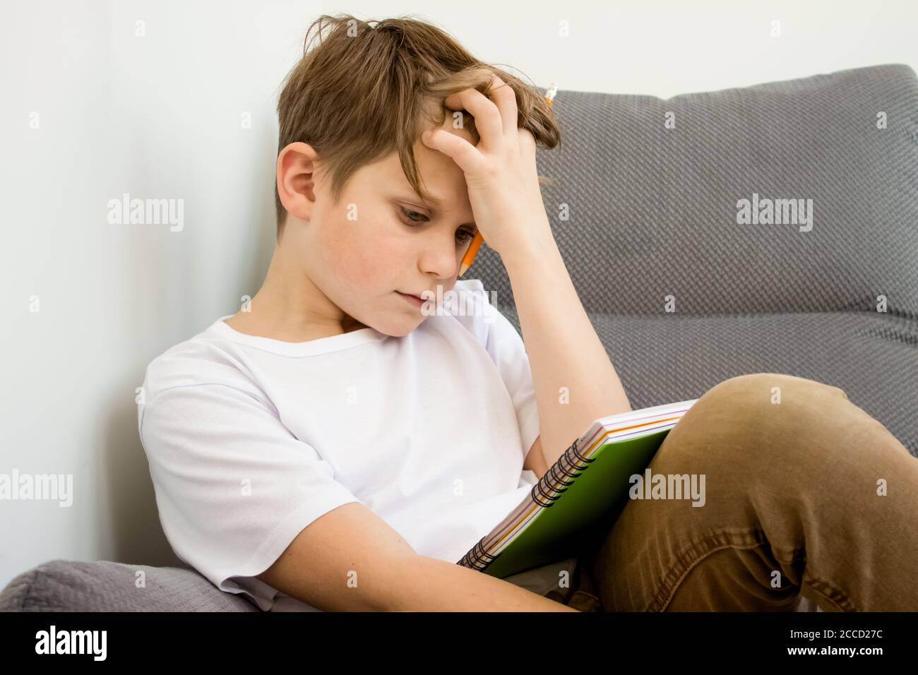 Müder Schuljunge arbeitet zu Hause kaum an seinen Hausaufgaben - Junge ist müde, frustriert und eingetaucht. Online-Studium zu Hause mit Büchern. Online-Schulungen Stockfoto