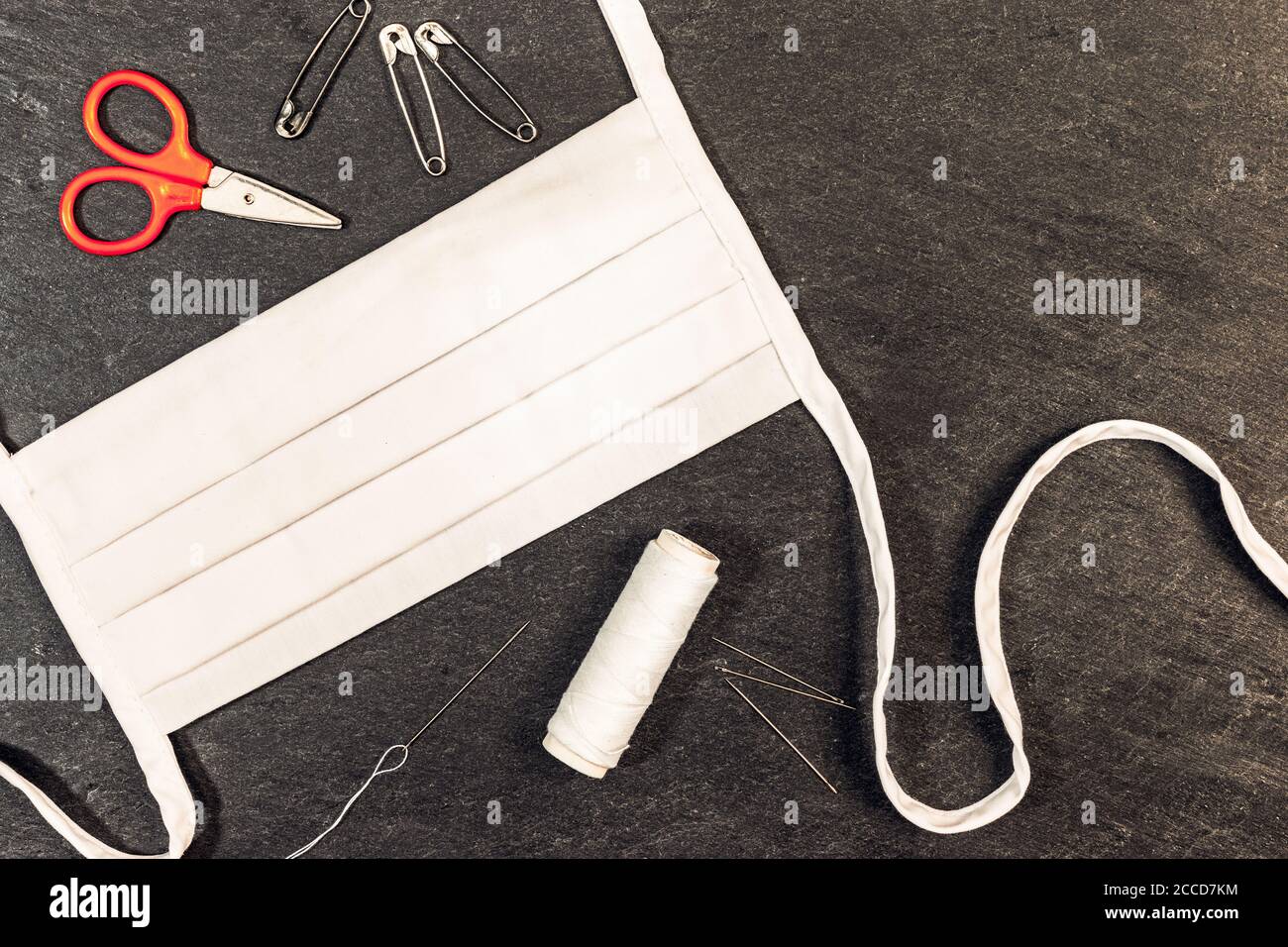 Hausgemachte weiße Baumwolle Gesichtsmaske mit Nadel und Faden auf einem dunklen Hintergrund mit Blick von oben. Stockfoto