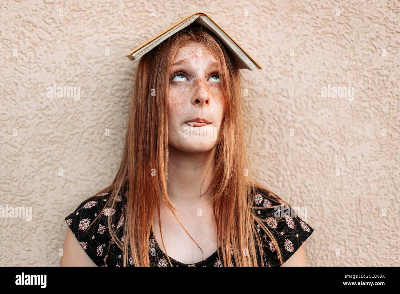 Teen Ingwer Student Mädchen mit einem Buch auf dem Kopf, Blick auf sie mit lustigen Gesichtsausdruck. Probleme beim Lernen, Schwierigkeiten Stockfoto