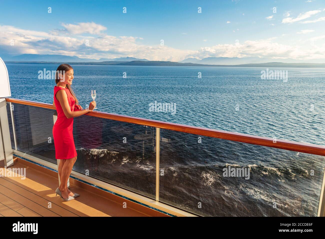 Kreuzfahrt Luxus Reise Lifestyle Frau auf Phantasie Europa Urlaub. Asiatische elegante Dame, die Champagner-Glas trinkt und den Sonnenuntergang auf der privaten Terrasse des Balkons beobachtet Stockfoto