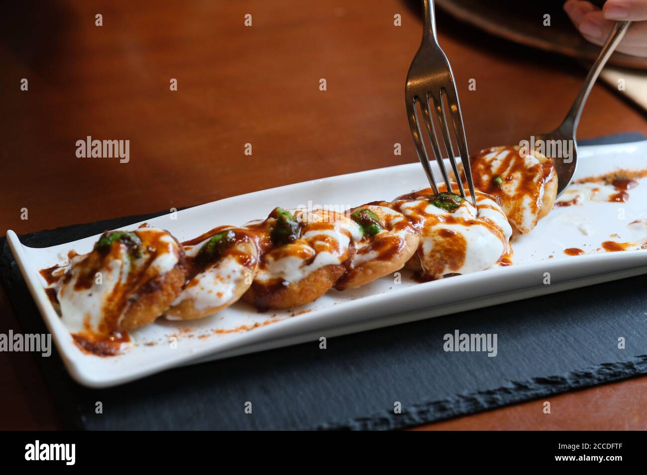 Nahaufnahme knusprig gebrannte Kartoffeln mit Joghurt und Minzsauce gekrönt. Traditionelle indische Küche. Unschärfe Hintergrund Stockfoto