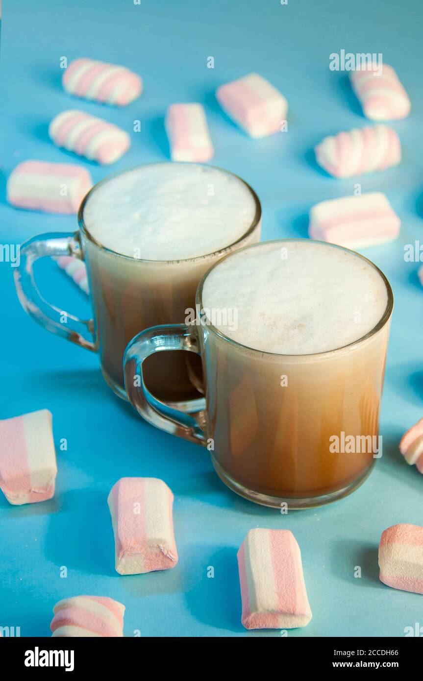 Weihnachts-Heißgetränk Kakao Kaffee oder Schokolade mit Milchcreme und Marshmallows in einer kleinen transparenten Tasse auf blauem Hintergrund. Winter. Neujahr Stockfoto