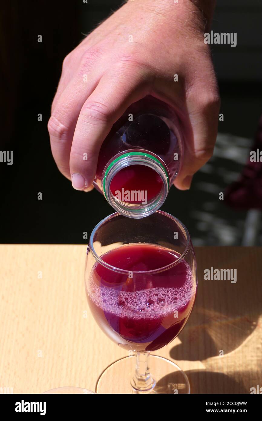 Nahaufnahme Hand Gießen aus roten Fruchtsaft oder Granatapfelsaft In einer Flasche in ein Glas auf einem Holztisch Stockfoto