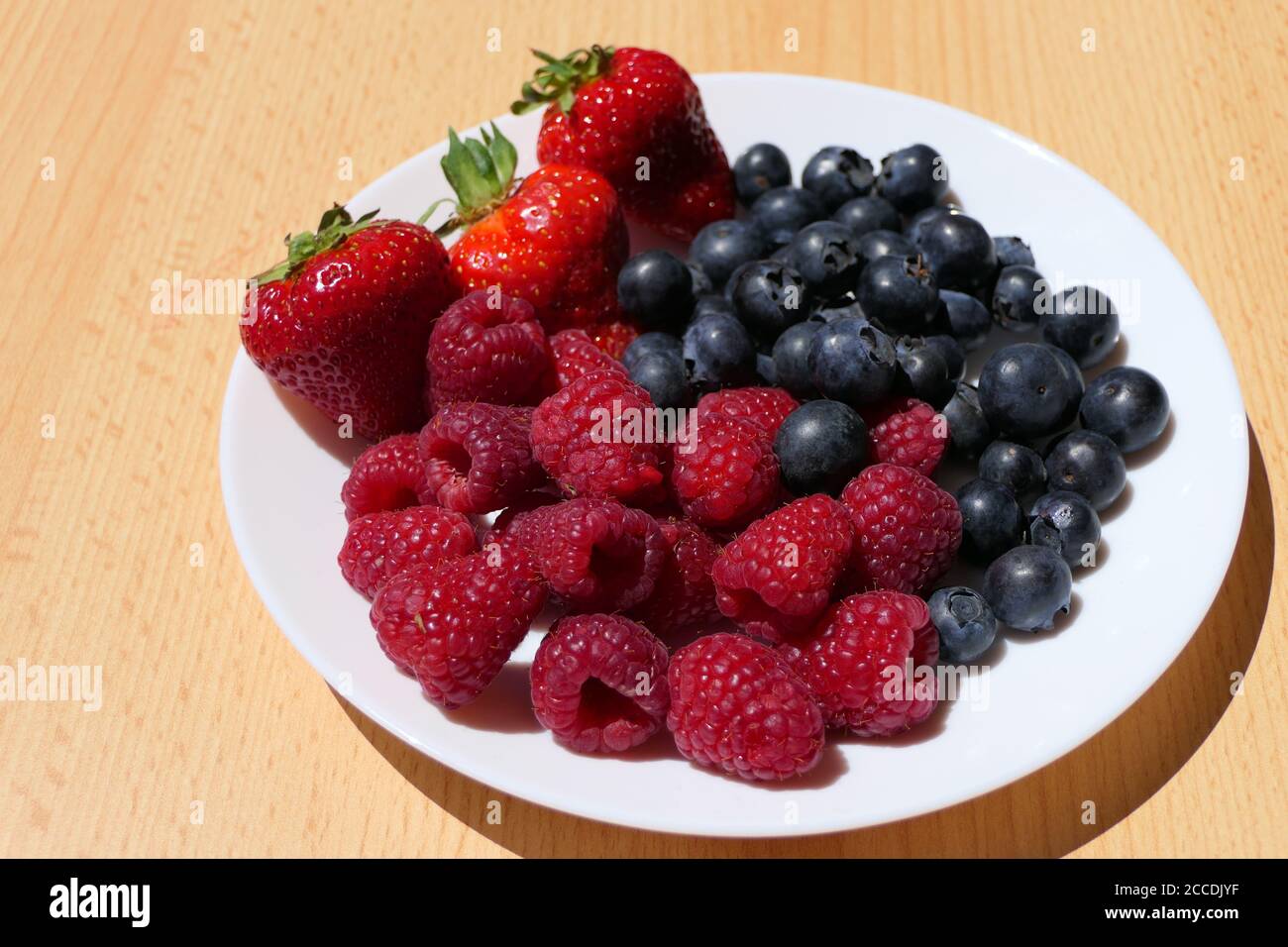 Weißer Teller mit gemischten Beeren einschließlich Erdbeeren, Himbeeren und Heidelbeeren auf einem Holztisch Stockfoto
