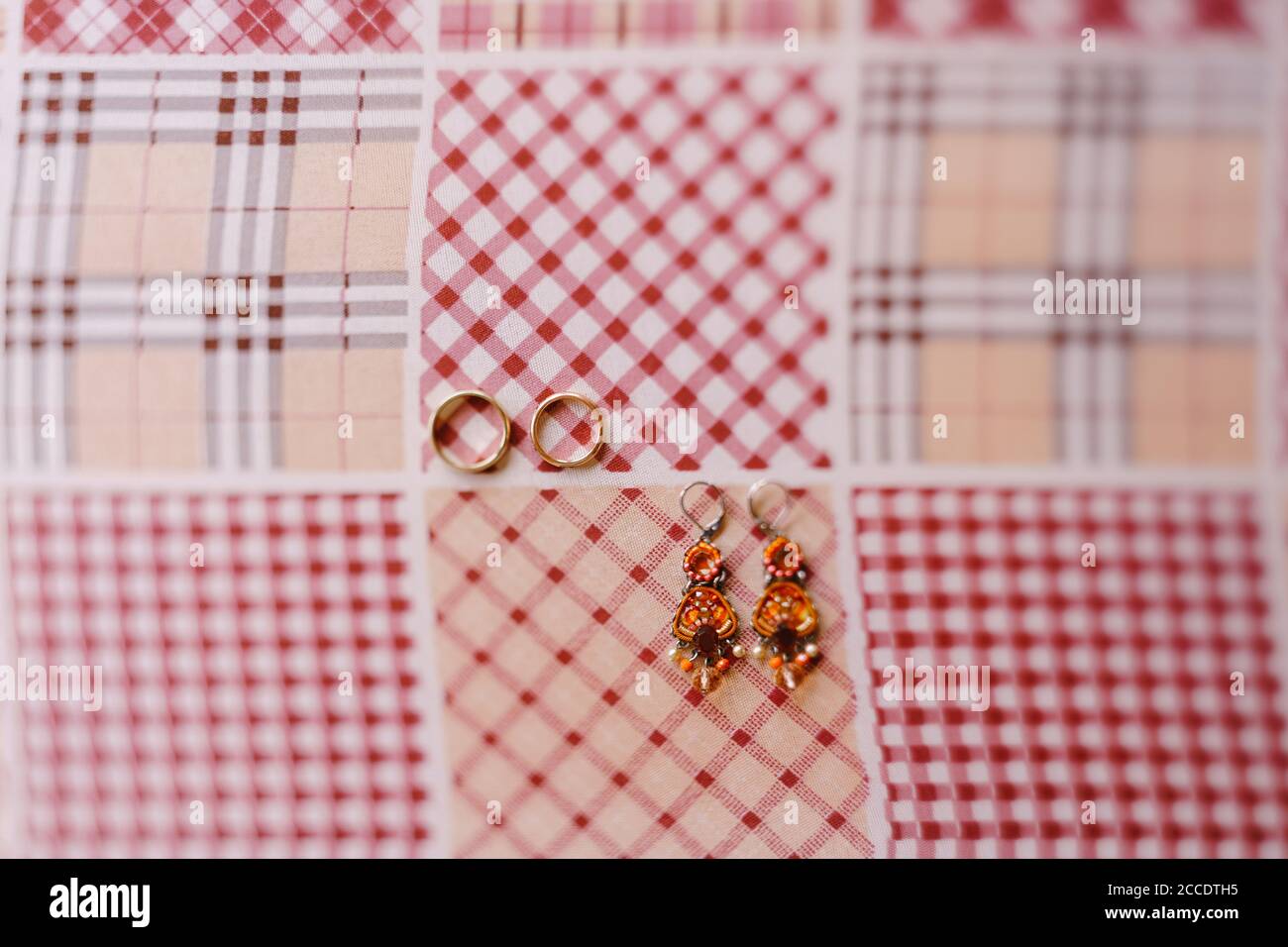 Budva, Montenegro - 21. august 2020: Nahaufnahme von Ohrringen mit Steinen und goldenen Eheringen auf kariertem Stoff. Stockfoto