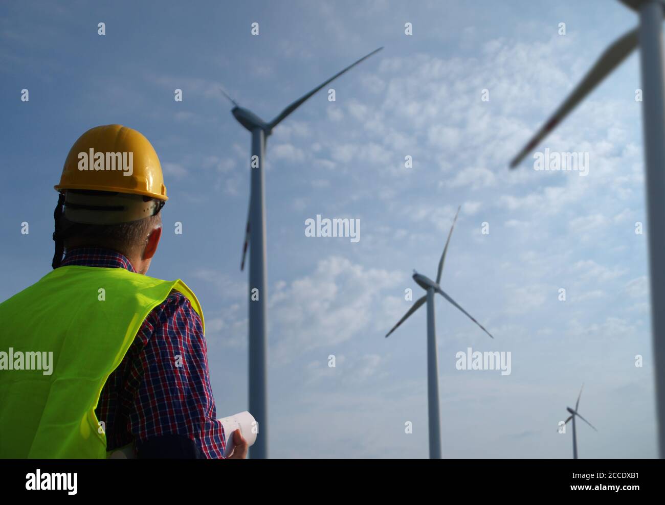 Ingenieur in einer Windenergieanlage. Ein Mann in einem Helm überwacht den Betrieb der elektrischen Windmühlen. Konzept für Ökologie und erneuerbare Energiequellen. Stockfoto