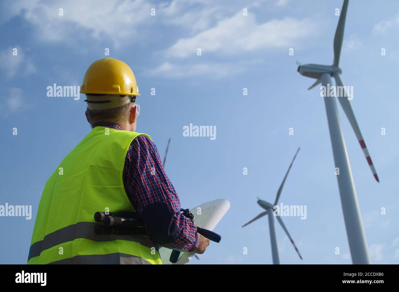 Ingenieur in einer Windenergieanlage. Ein Mann in einem Helm überwacht den Betrieb der elektrischen Windmühlen. Konzept für Ökologie und erneuerbare Energiequellen. Stockfoto