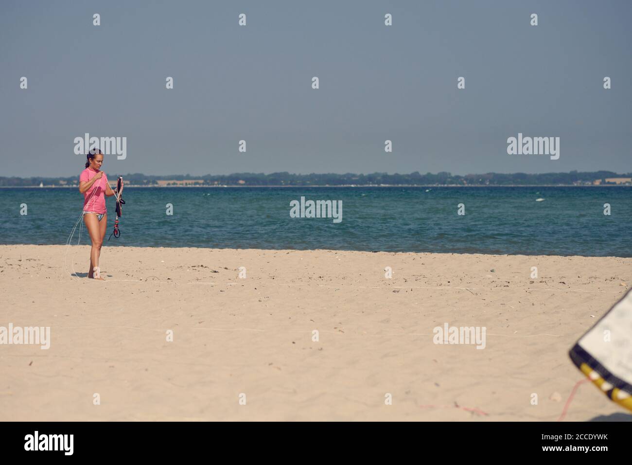 Frau mittleren Alters bereitet einen Drachen auf einem tropischen Strand für Surfen an einem heißen Sommertag in ihrem Jahresurlaub Stockfoto