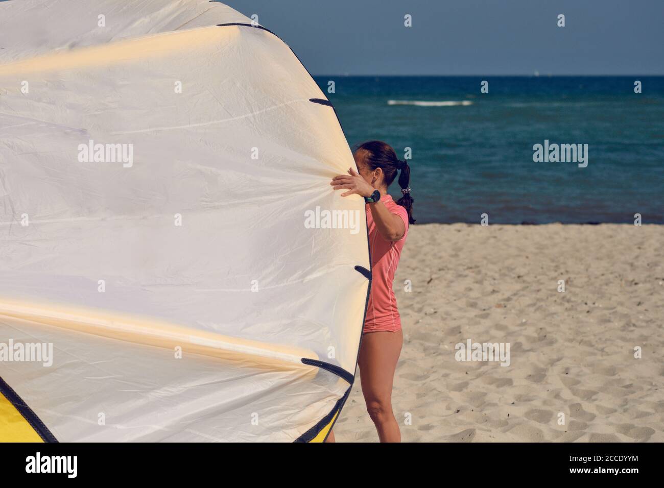 Junge Frau am Meer mit großen bunten Drachen oder Kitesurfen Segeln steht auf einem sandigen Sommerstrand in Ihr Schwimmkostüm Stockfoto
