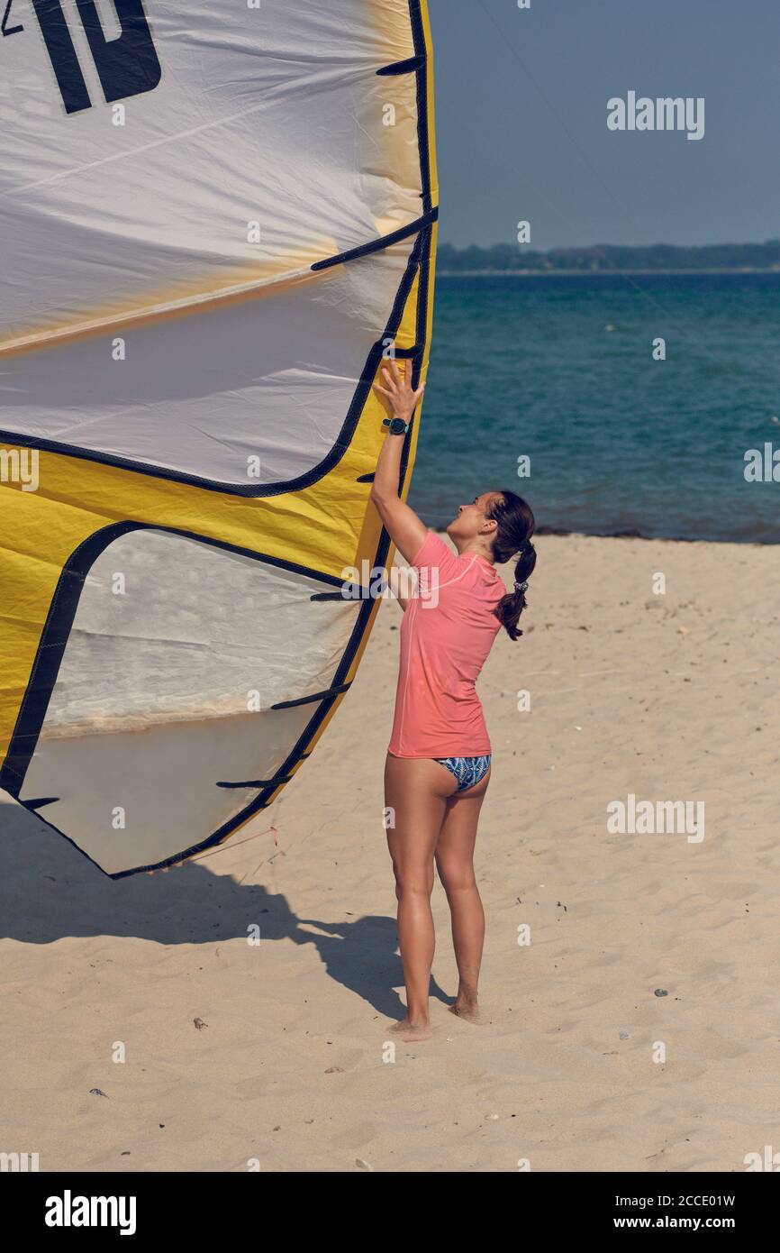 Junge Frau am Meer mit großen bunten Drachen oder Kitesurfen Segeln steht auf einem sandigen Sommerstrand in Ihr Schwimmkostüm Stockfoto