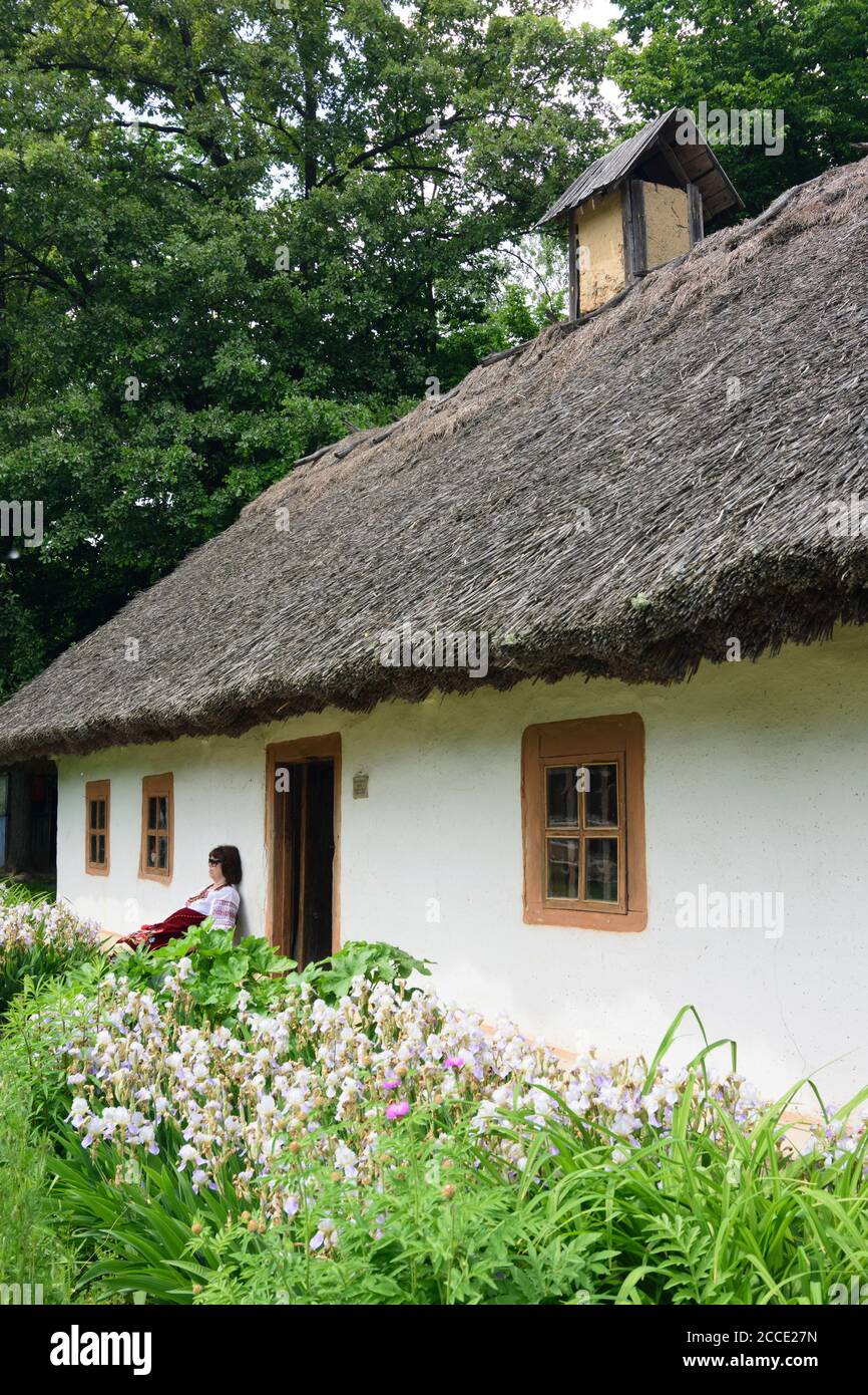 Kiew (Kiew), Museum für Volksarchitektur und Volkswege der Ukraine in Pyrohiv, Holzhaus, Strohdach, Museumswärter in traditioneller Kleidung in K Stockfoto