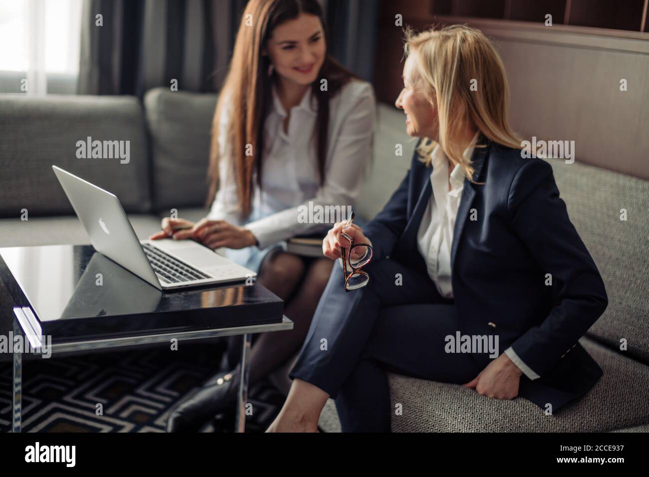 Konzept für kleine Unternehmen. Junge kreative Kleinunternehmen arbeiten mit neuen Startup-Projekt im modernen Büro. Zwei junge Frauen sitzen auf dem Sofa und Stockfoto