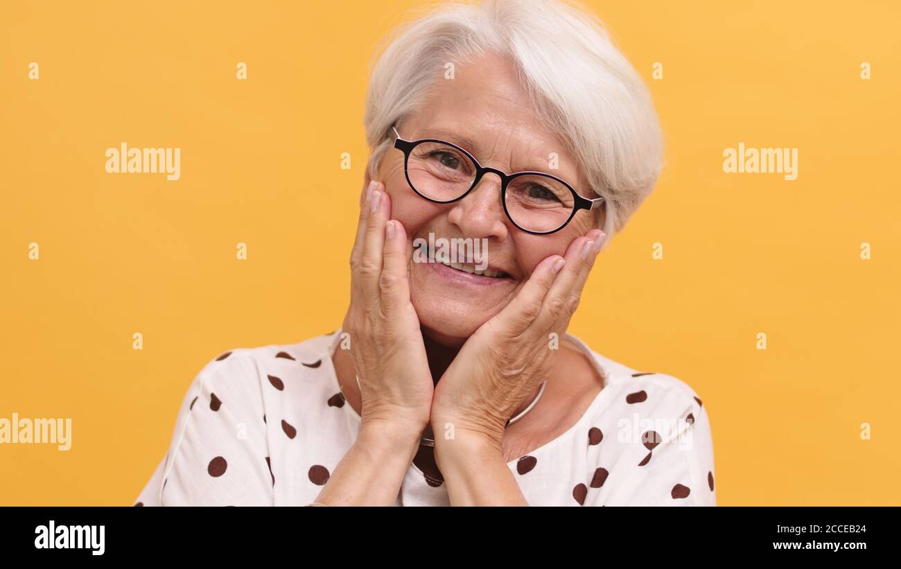 Porträt einer emotional lächelnden älteren Frau, die ihre Hände an ihren Wangen hält. Hochwertige Fotos Stockfoto