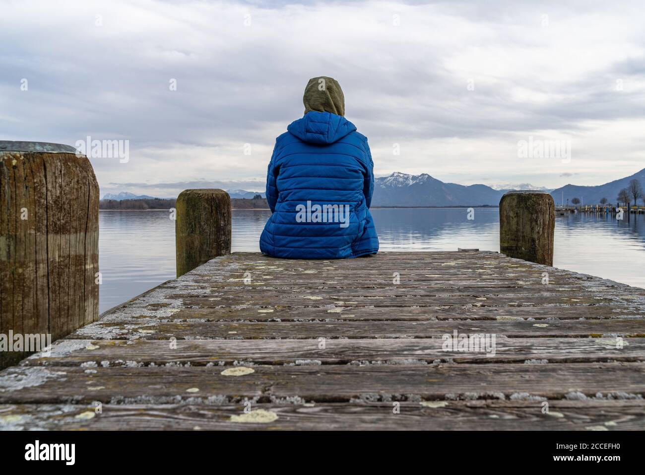 Europa, Deutschland, Bayern, Rosenheim, Prien am Chiemsee, Chiemsee, Mann sitzt auf dem Steg und blickt über den Chiemsee zu den Chiemgauer Alpen Stockfoto