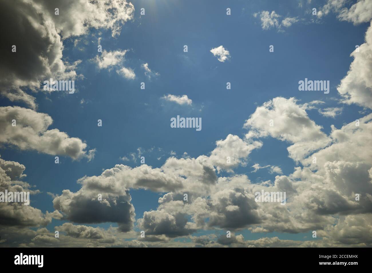 Wolken schweben über dem blauen Himmel, die von Sonnenstrahlen erhellt werden. Heller Sommertag. Hintergrund für Vorhersage und Meteorologie Illustration Stockfoto