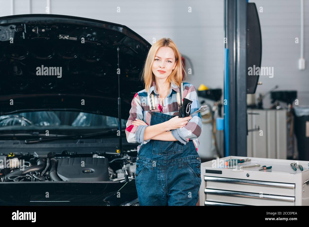 Angenehme attraktive blonde selbstbewusste Mechaniker stehen vor dem kaputten Auto, Nahaufnahme Porträt. Hobby, Beruf Stockfoto