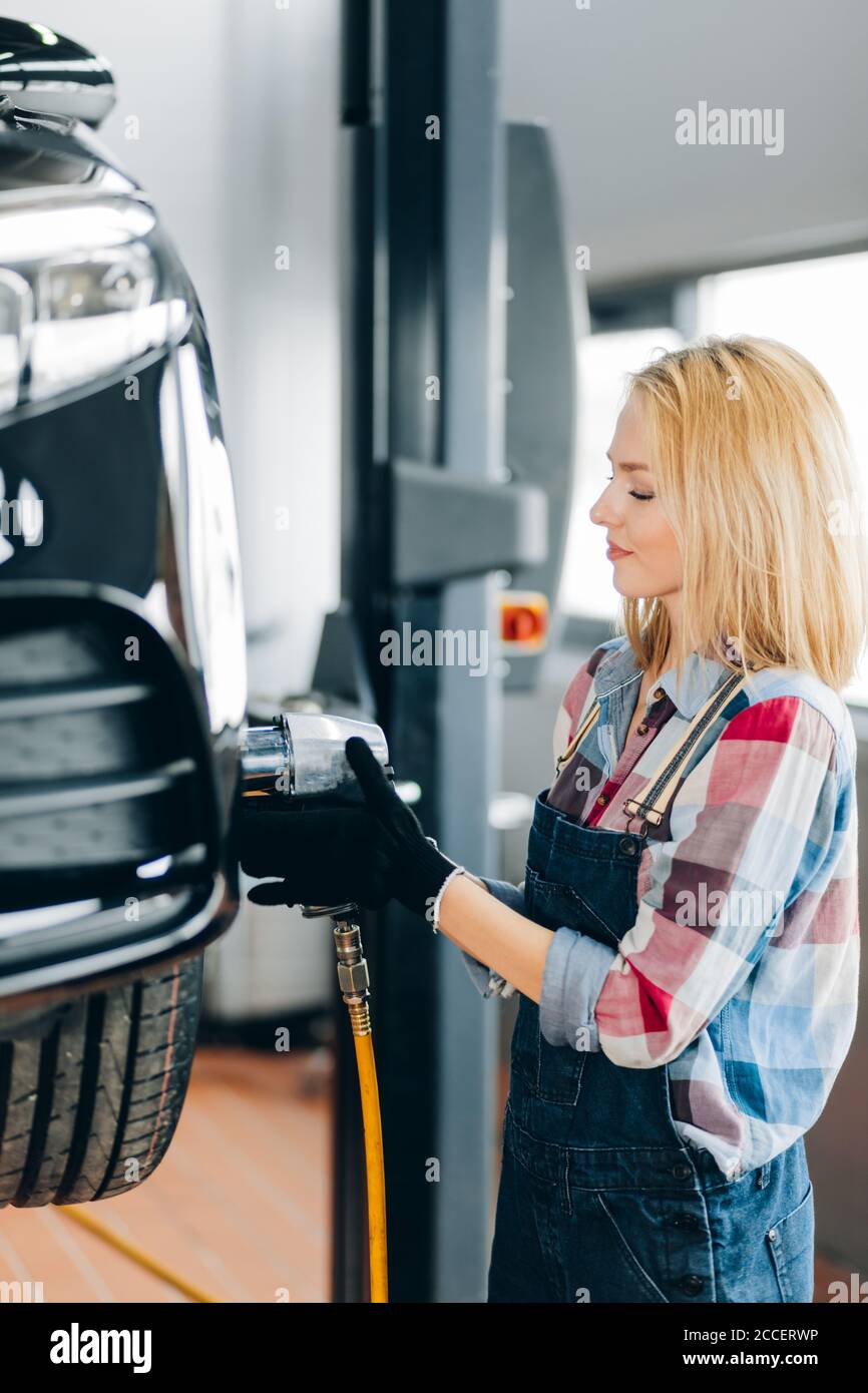 Glücklich talentierte professionelle Mechaniker arbeiten mit Schlagschrauber des angehobenen Automobils in der Garage. Nahaufnahme Seitenansicht Foto. Lifestyle Stockfoto